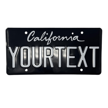California license plate. The top one is a black and white license plate with a cursive "California" writing. The license plate spells out "YOURTEXT". 